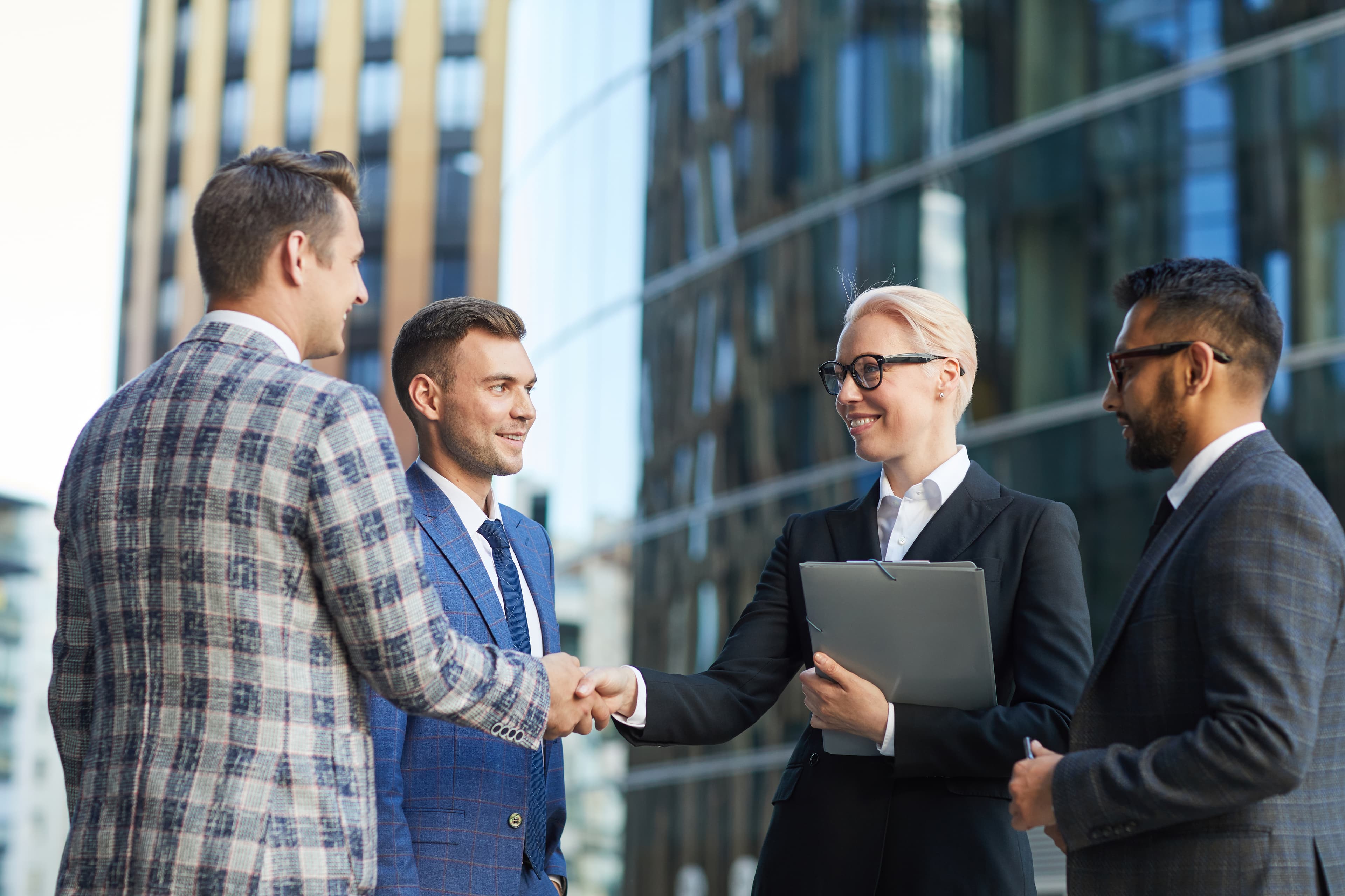 Professionals shaking hands outside an office tower.